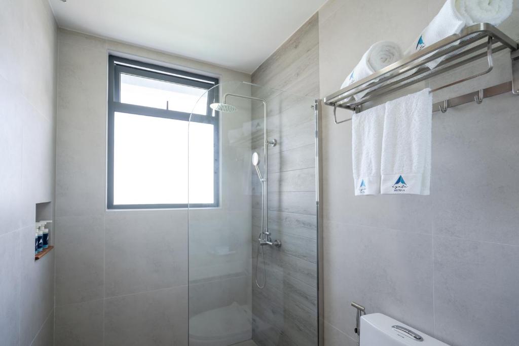 Mūsdienīgs dušas telpa ar stikla kabīni, logu un tīriem dvieļiem uz plaukta. Interjers ir veidots ar gaišām flīzēm un minimālisma dizainu.