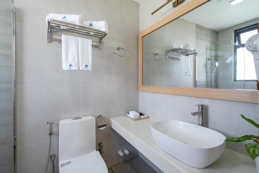 Mūsdienīgs vannasistabas interjers ar elegantu izskatu, tostarp balto izlietni un lielu spoguli. Telpā redzami dvieļi un dušas stūrītis.