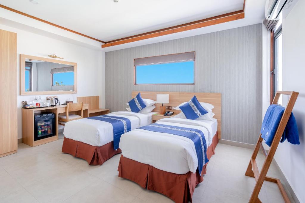 Mūsdienīgs viesnīcas numurs ar divām atsevišķām gultām, koka mēbelēm un dabisku apgaismojumu. Numurā ir galdiņš, krēsli un mini ledusskapis.