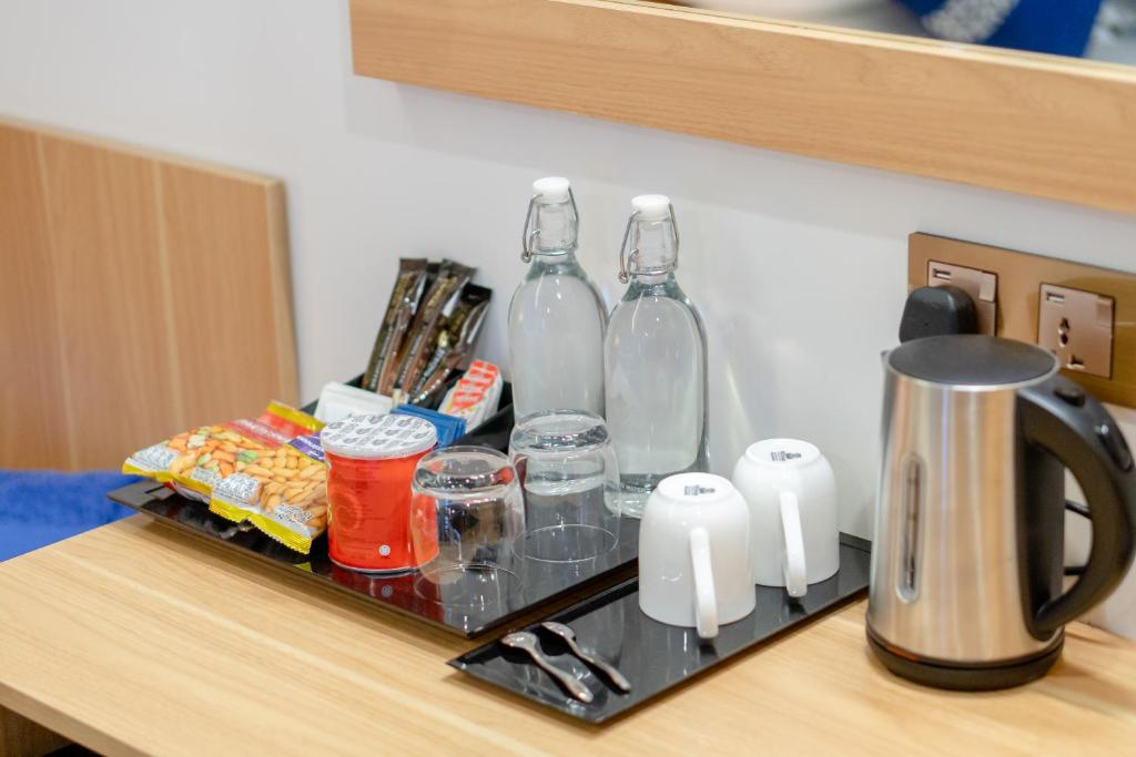 Kafijas un tējas stacija viesnīcas numurā ar ūdens pudelēm, glāzēm, uzkodām un tējkannu.