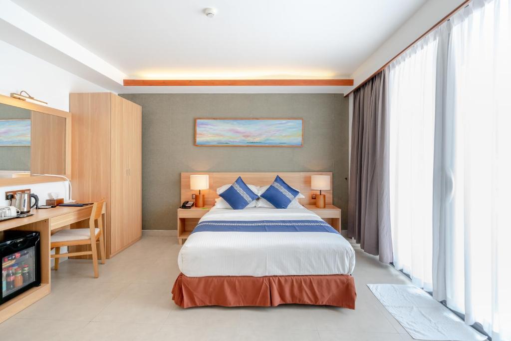 Mūsdienīga viesnīcas numura iekārtojums ar gultu, koka mēbelēm un dabīgu apgaismojumu. Interjeru papildina mīkstie toņi un mākslas darbs uz sienas.