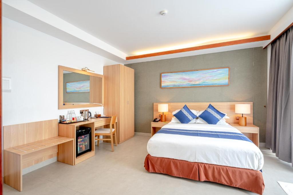 Mūsdienīga viesnīcas istaba ar divguļamo gultu, koka mēbelēm un gaismas elementiem. Istabā ir rakstāmgalds, ledusskapis un spogulis, radot komfortablu atmosfēru.