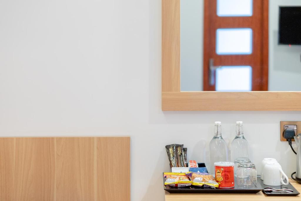 Mūsdienīgas viesnīcas numura daļa ar spoguli, galdautu un dažādiem dzērieniem un uzkodām. Redzama arī koka siena un durvis uz citu telpu.