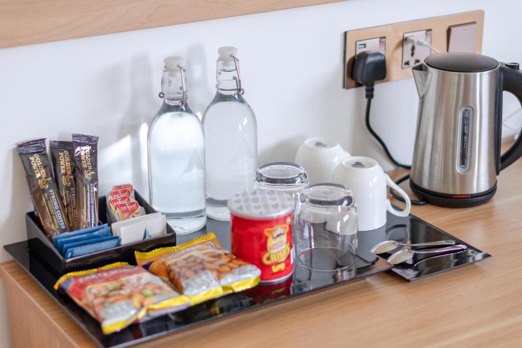 Kafijas stūra komplekts ar ūdens pudelēm, kafijas maisījumiem, uzkodām un tējas tases. Ideāli piemērots relaksācijai viesnīcā.