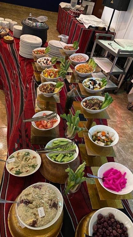 Bagātīgs ēdienu galds ar dažādām uzkodām un salātiem, kas pasniegti tradicionālā galda klājumā. Redzami arī dažādu salātu un mērču trauki, kas papildina maltīti.