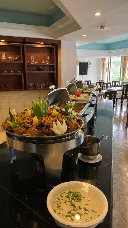 Bagātīgs bufete ar dažādiem ēdieniem, tostarp gaļas un dārzeņu uzkodām, rotātas ar ziediem un garnējumiem. Restorāna interjers ir gaišs un viesmīlīgs.