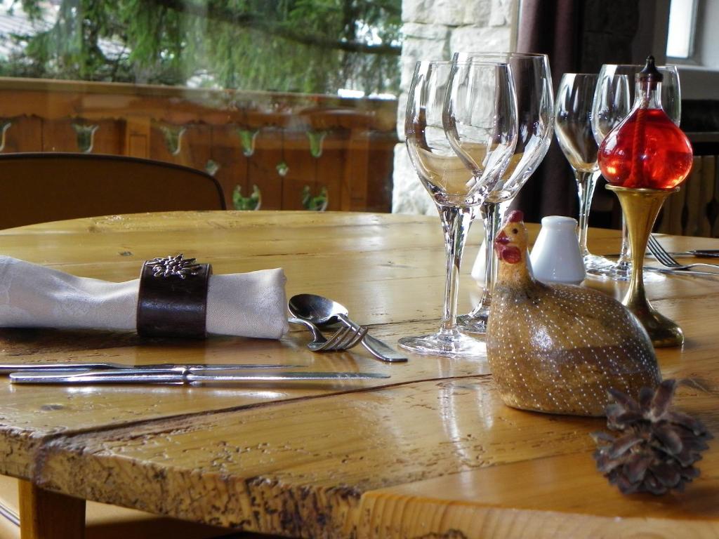 Galda uzstādījums ar glāzēm, sudraba galda piederumiem un dekoratīvu putnu figūriņu, radot mājīgu atmosfēru.