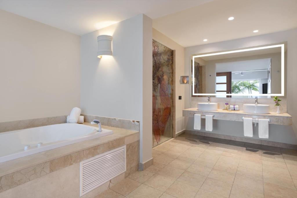 Mūsdienīgs un elegants vannas istabas interjers ar džakuzi, divām izlietnēm un lielu spoguli, apgaismojuma elementiem un dabīgu gaismu no loga.