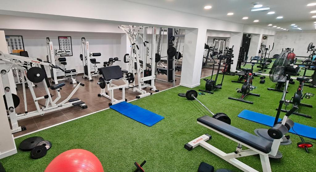 Sporta zāle ar dažādiem trenažieriem un svaru aprīkojumu, kā arī zaļā zāliena grīda, kas rada dinamisku un motivējošu vidi treniņiem.