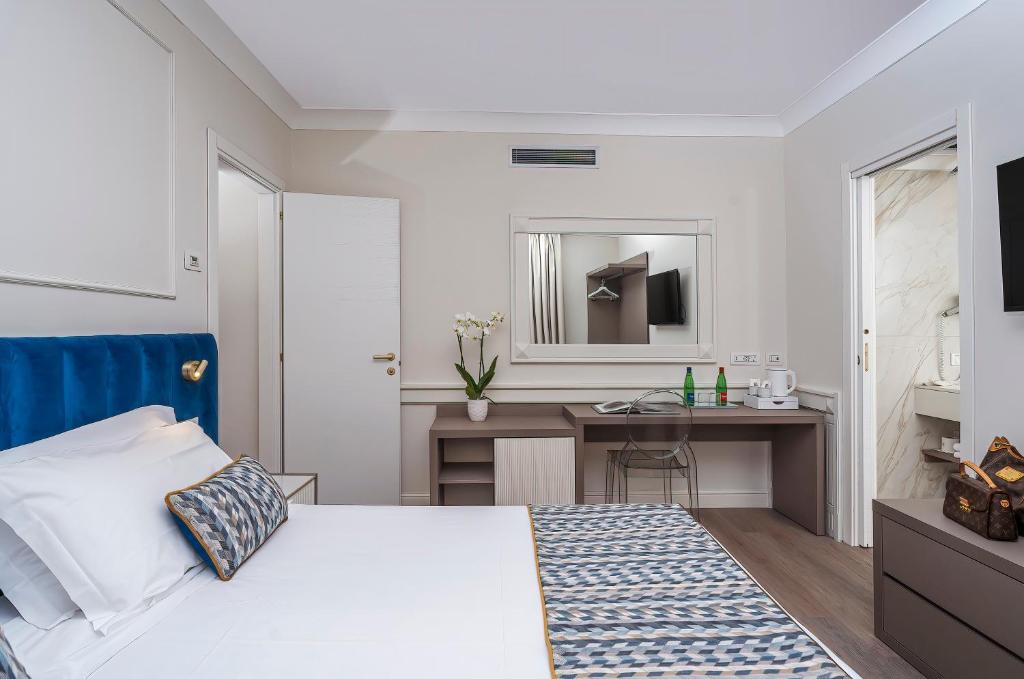 Mūsdienīgs viesnīcas numurs ar zilu gultas pārklāju, galdu un krēslu, kā arī vannas istabu blakus. Numurā ir televizors un spogulis.