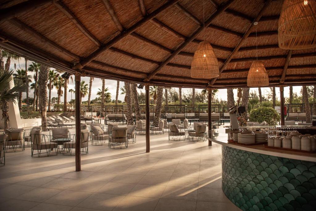 Tropu stila restorāns ar atvērtu telpu, elegantiem mēbeļiem un dabīgu apgaismojumu, kas rada relaksējošu atmosfēru. Apkārt ir palmām un atpūtas zonām, kas piešķir viesmīlīgu noskaņu.