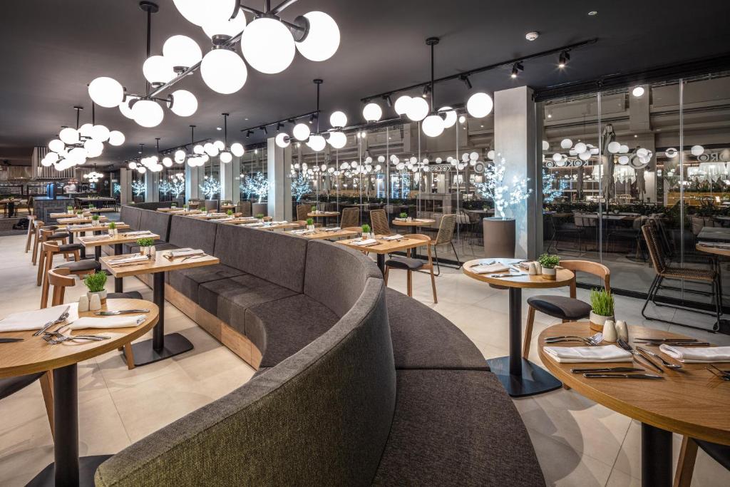 Mūsdienīgs restorāns ar elegantu apgaismojumu un stilīgu interjeru, kas ietver koka galdiņus un ērtas sēdvietas. Gaismas un augi rada patīkamu atmosfēru.