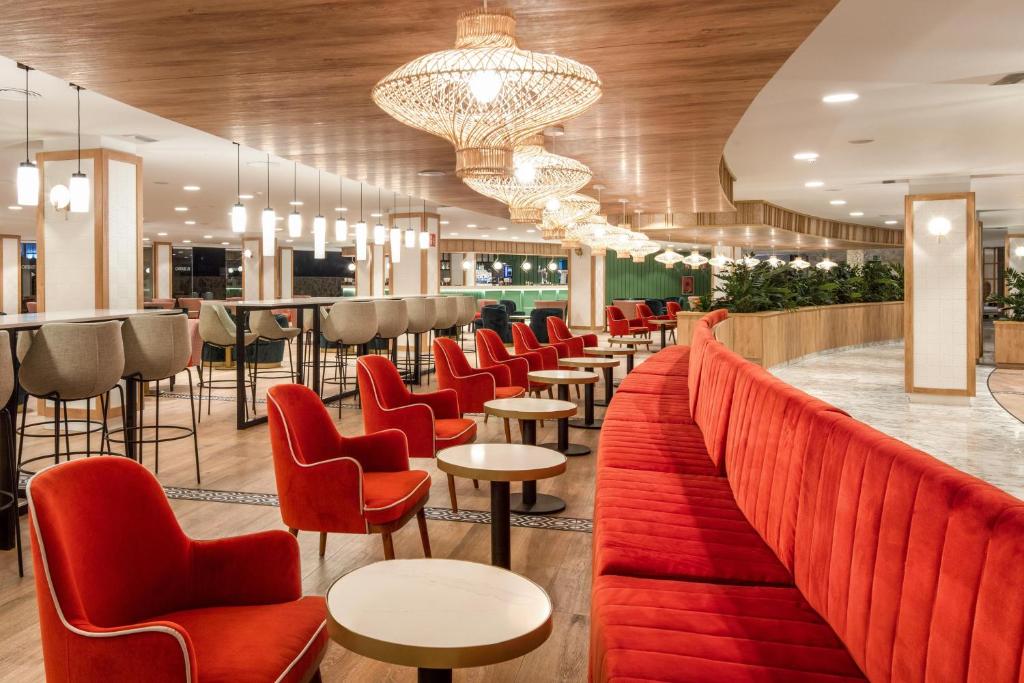 Mūsdienīgs bārs ar sarkaniem krēsliem un elegantām lampām, kas rada siltu atmosfēru. Interjers apvieno koka un akmens elementus, piedāvājot patīkamu atpūtas vietu.