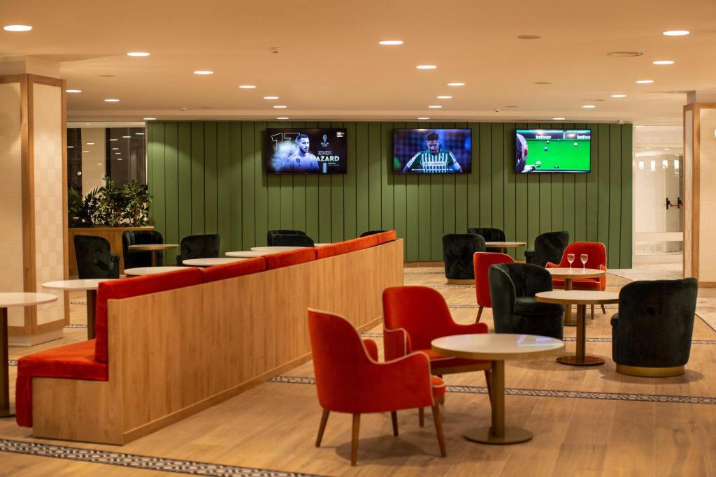 Mūsdienīga atpūtas zona ar komfortablām sēdvietām un televizoriem, kur tiek rādīti sporta notikumi. Siltas krāsas un augu elementi piešķir telpai viesmīlīgu atmosfēru.