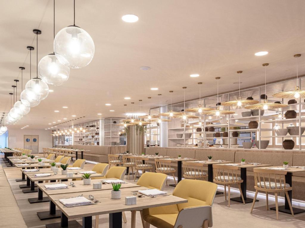 Mūsdienīgs restorāns ar elegantu iekārtojumu, kurā redzami koka galdi un dzeltenas krēsli. Gaismas ķermeņi rada patīkamu atmosfēru, savukārt plaukti ar traukiem piešķir papildus stilu interjeram.