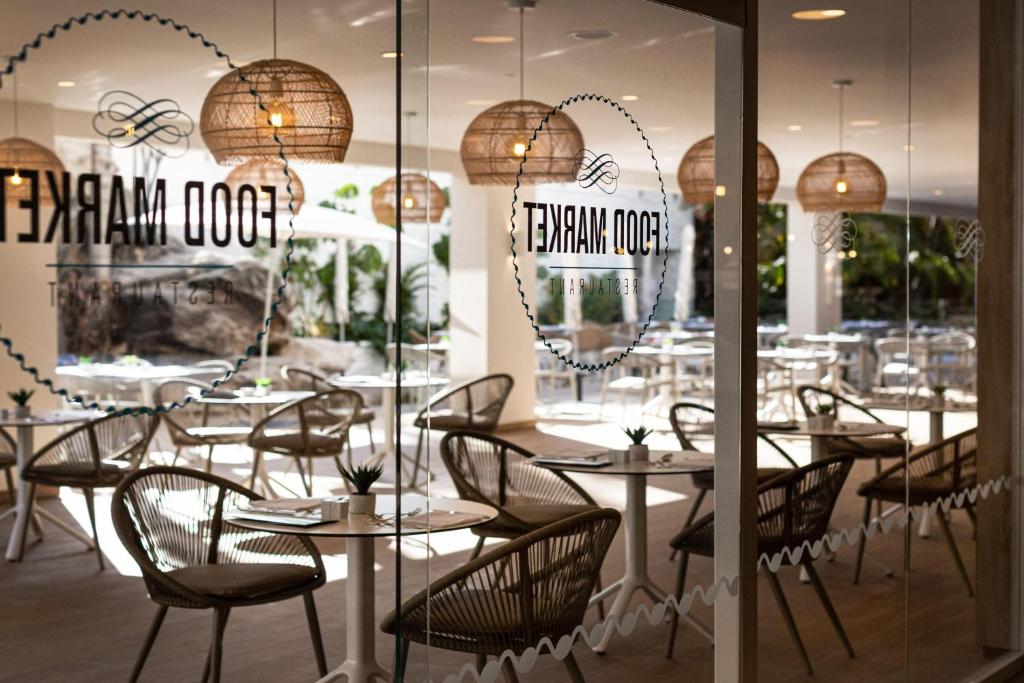 Restorāna "Food Market" iekārtojums ar modernām mēbelēm un apgaismojumu, redzams caur stikla durvīm. Eleganta atmosfēra ar viesmīlīgu un mājīgu dizainu.