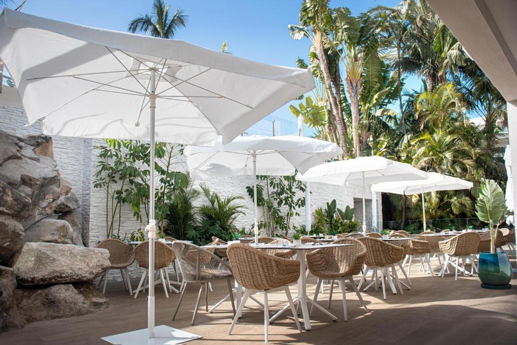 Āra ēdināšanas zona ar baltiem lietussargiem un vītņu krēsliem, ko ieskauj zaļumi un palmām. Ideāla vieta relaksācijai un maltītēm svaigā gaisā.