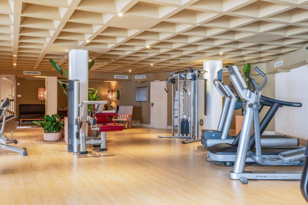 Mūsdienīga trenažieru zāle ar dažādiem sporta aprīkojumiem un zaļām augiem. Telpa ir gaiša un plaša, radot patīkamu vidi treniņiem.