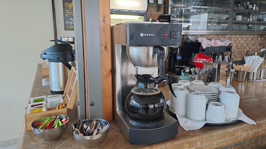 Kafijas automāts ar tējkannu un kafijas traukiem, izvietots kafejnīcā, blakus garšvielām un galda piederumiem. Ideāla vide kafijas baudīšanai.