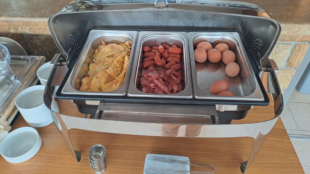 Siltā ēdienu bufete ar omleti, desiņām un vārītiem olu šķīvjiem, kas izkārtoti metāla traukos.