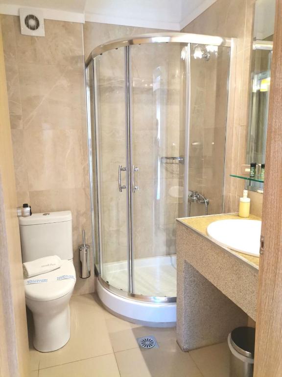 Mūsdienīga vannas istaba ar stikla dušas kabīni, tualeti un izlietni. Interjers veidots ar neitrālām krāsām un elegantu akmeņu apdari.