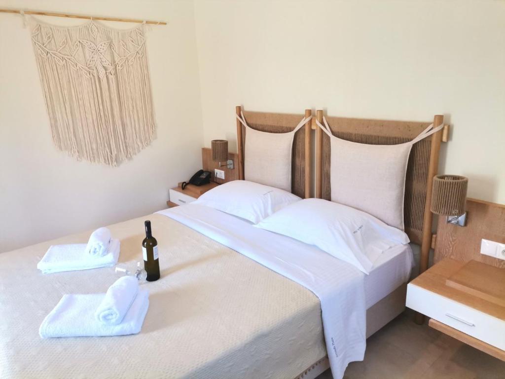 Mūsdienīgs guļamistabas interjers ar gultu, papildināts ar baltām dvielēm un vīna pudeli uz naktsgaldiņa. Sienā redzams dekoratīvs makramē izstrādājums, kas piešķir telpai siltumu un stilu.