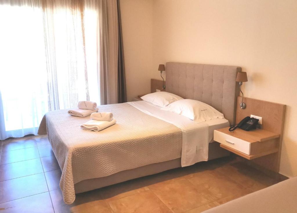 Mūsdienīga viesnīcas numura interjers ar divguļamo gultu, spilveniem un naktsgaldiņu, blakus logam ar aizkariem. Numurs ir gaišs un ērts, ideāli piemērots atpūtai.