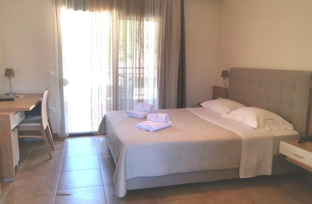 Mūsdienīga viesnīcas istaba ar divguļamo gultu, rakstāmgaldu un logiem, caur kuriem ieplūst dabiska gaisma. Gultas veļa ir sakopta, un uz gultas ir salocītas dvieļi.