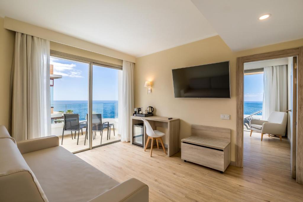 Grezna viesnīcas numura iekārtojums ar skatu uz jūru, moderns televizors un balkons. Numurā ir ērtas mēbeles un gaisīgas aizkaru, kas rada patīkamu atmosfēru.