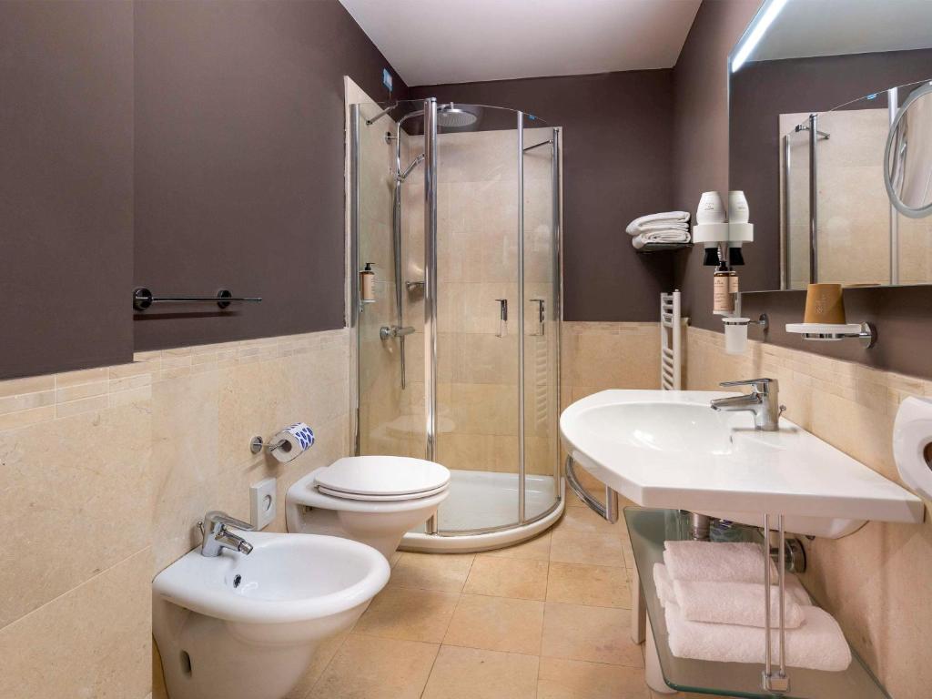 Mūsdienīgs vannas istabas interjers ar dušas kabīni, izlietni un bidē, apgaismots ar siltu gaismu, radot ērtu atmosfēru.