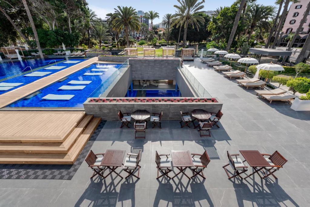 Elegants baseins ar zilu ūdeni un sauļošanās krēsliem, apzaļumota teritorija ar palmām un atpūtas zonām. Ideāla vieta atpūtai un relaksācijai.