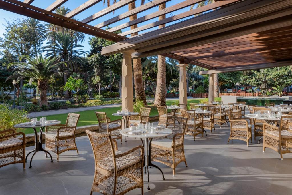 Āra restorāna terase ar vītņu krēsliem un galdiņiem, gleznainā vidē ar palmām un zaļu dārzu. Ideāla vieta relaksācijai un ēdiena baudīšanai.