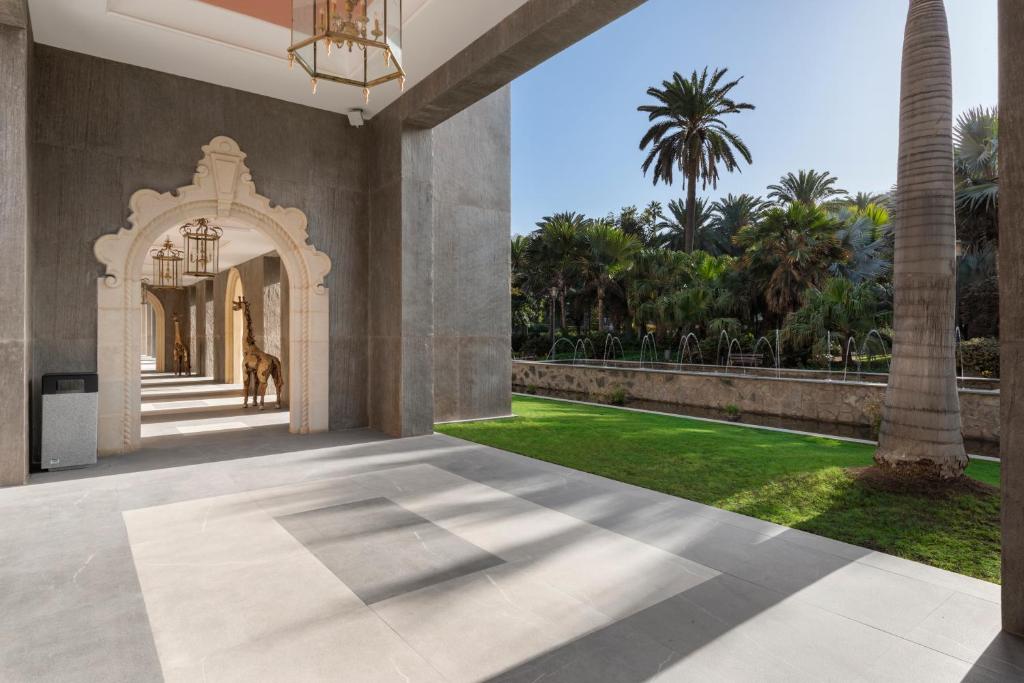 Mūsdienīgs un elegants arhitektūras elements ar izteiksmīgu arku un gaismas ķermeņiem, kas vērsts uz ainavu ar zaļojošiem palmu kokiem un dārzu. Šī telpa rada mierīgu atmosfēru un harmoniju.