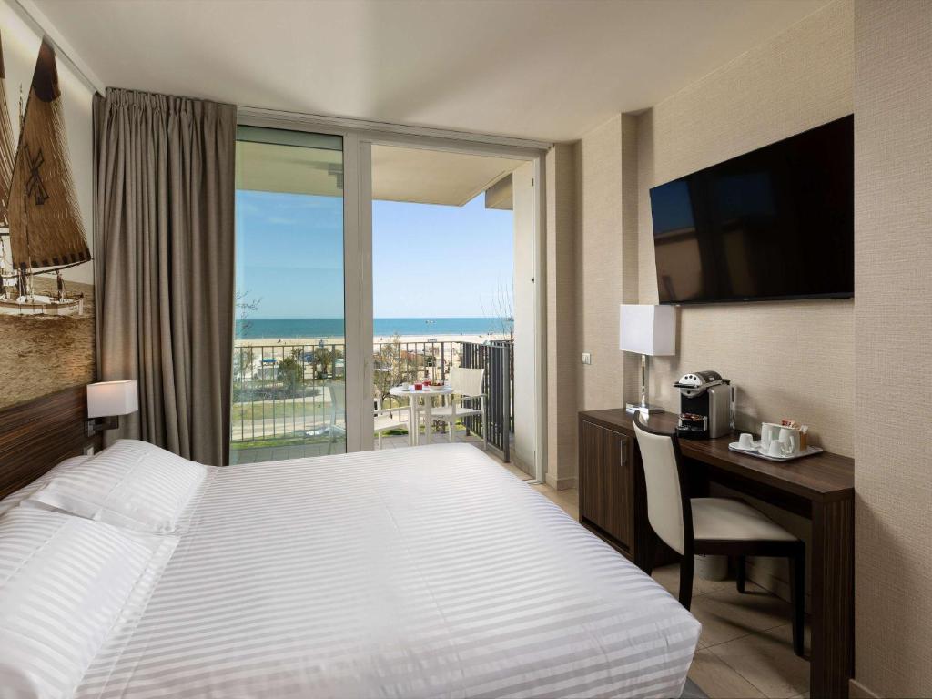 Mūsdienīga viesnīcas numura iekšskats ar skatu uz jūru, aprīkots ar televizoru, rakstāmgaldu un kafijas automātu. Numurs ir gaišs un gaumīgi iekārtots, radot komfortablu atmosfēru.