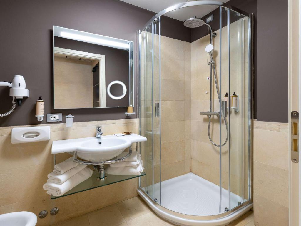 Mūsdienīgs vannas istabas interjers ar stikla dušas kabīni, izsmalcinātu izlietni un modernu spoguli. Svaigas dvieļi un higiēnas piederumi papildina telpas eleganci.