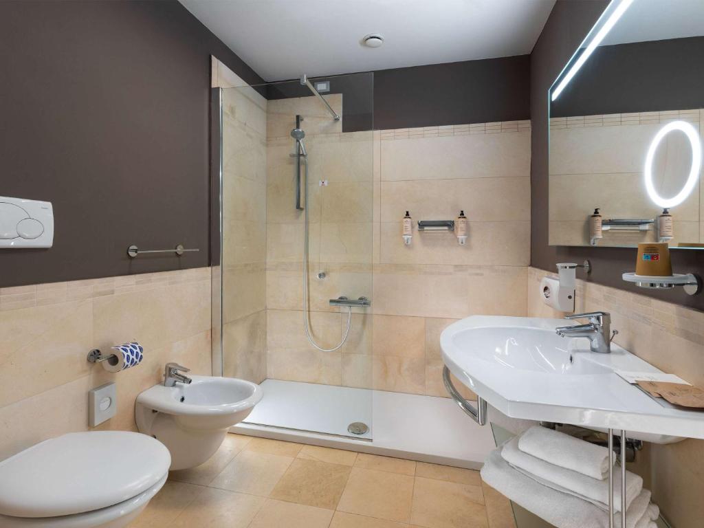 Mūsdienīga vannas istaba ar stikla dušu, mūsdienīgu izkārtojumu un dabīgiem toņiem. Tajā ir izsmalcināti sanitārie elementi un labi organizēti higiēnas piederumi.