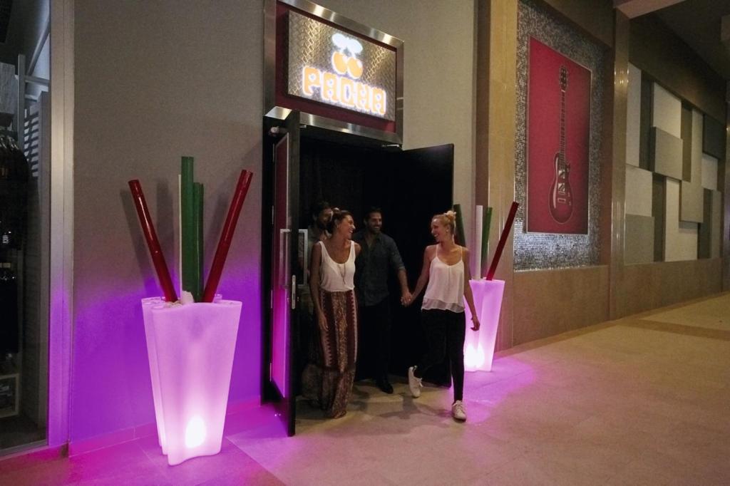 Divi cilvēki izej no naktskluba, kas ir apgaismots ar rozā gaismu, un blakus ir stilīgas dekorācijas. Ievērojama naktsdzīves atmosfēra.