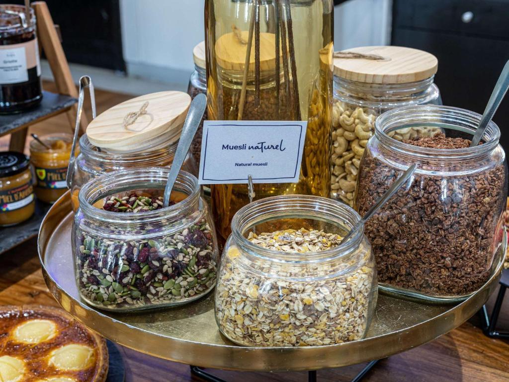 Dabīgais muslis ar dažādiem graudiem un riekstiem, izkārtots stikla burkās uz zelta krāsas paplātes.