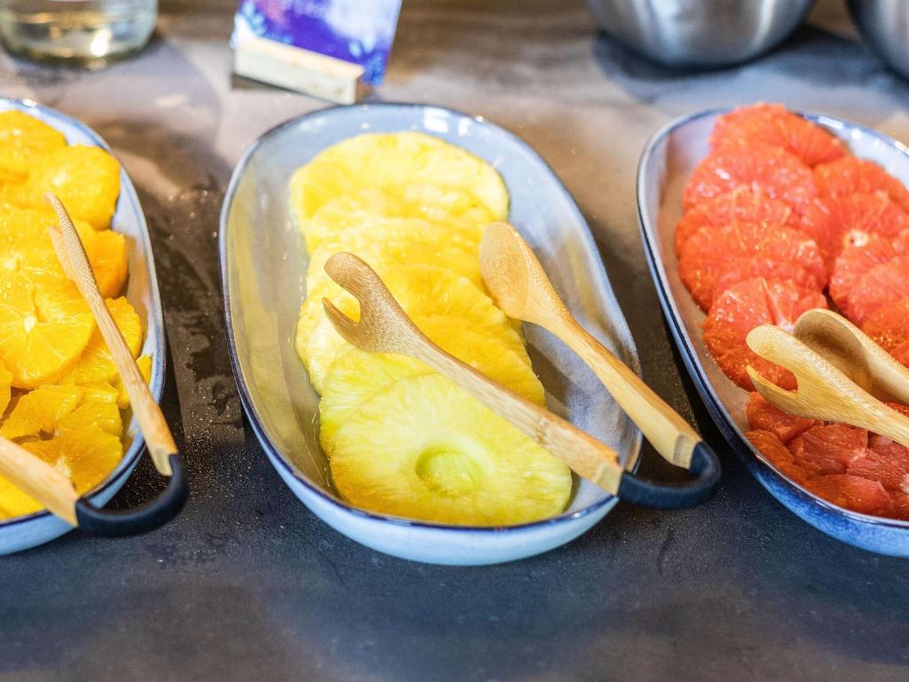 Svaigu augļu salikums uz pandēm, ietverot apelsīnus, ananāsus un greipfrūtus, ar koka karotēm pasniegšanai.