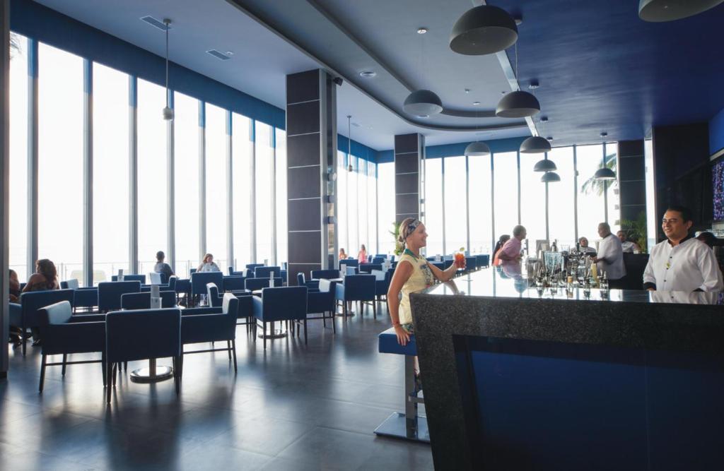 Moderns bārs ar plašiem logiem, kas nodrošina dabiski apgaismotu telpu. Klienti bauda dzērienus, kamēr apkalpojošais personāls strādā aiz bāra.