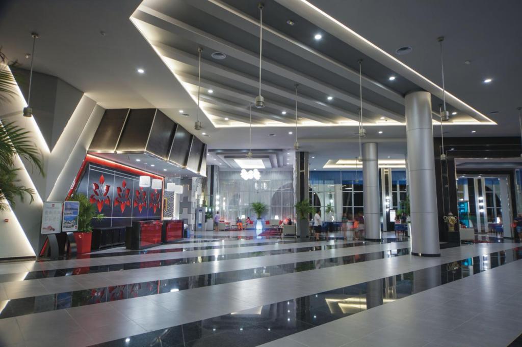 Mūsdienīgs viesnīcas vestibils ar elegantu apgaismojumu un stilīgu interjeru, kas ietver melnus un baltus flīzes, kā arī dekoratīvas augu rotājumus.