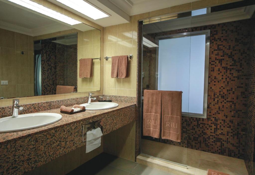 Mūsdienīga vannas istaba ar divām izlietnēm un granīta virsmu, kurā ir pāris dvieļu un stiklota duša. Sienas ir dekorētas ar mozaīkas flīzēm, radot elegantu atmosfēru.