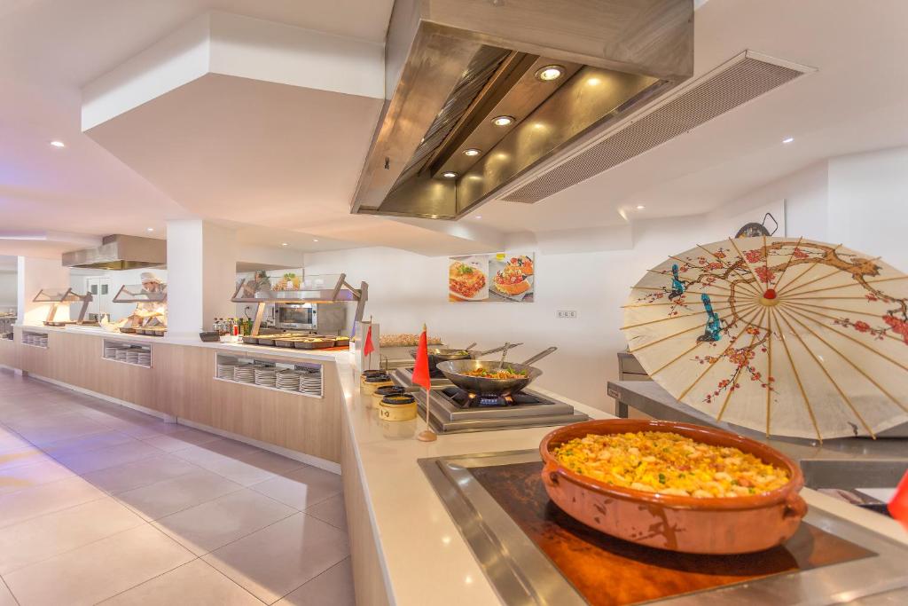 Mūsdienīgs restorāns ar atvērtu virtuvju, kur tiek piedāvāti dažādi ēdieni. Interjerā redzams dekoratīvs lietussargs un vairāki ēdienu gatavošanas stendi.