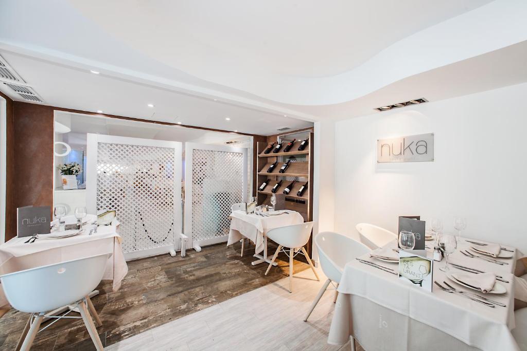 Mūsdienīgs restorāns ar elegantiem galdiem, kas dekorēti ar baltiem galdautiem, un vīna plauktu uz sienas. Interjers ir gaišs un stilīgs, radot patīkamu atmosfēru.