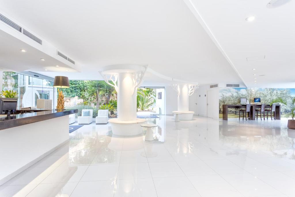 Mūsdienīgs viesnīcas interjers ar gaišām krāsām, elegantu reģistratūru un zaļo dārzu fonā. Atvērta telpa ar stilīgiem mēbeļu elementiem un daudz gaismas.