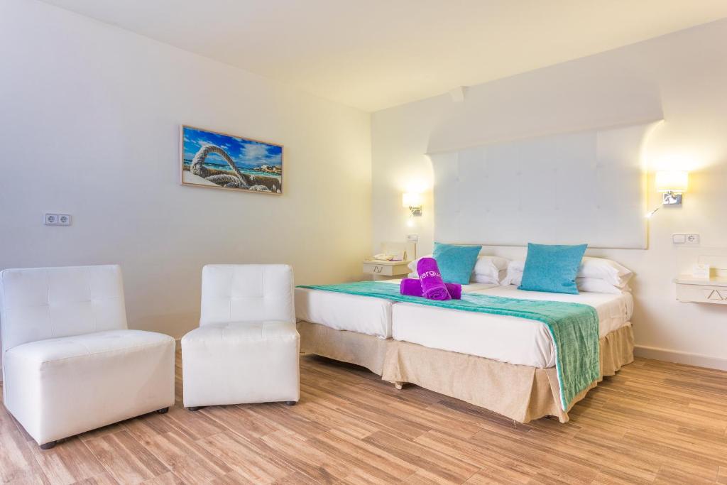 Mūsdienīgs viesnīcas numurs ar divām gultām, baltām krēslām un krāsainiem dvieļiem. Sienā ir gleznaina ainava, kas piešķir telpai patīkamu atmosfēru.