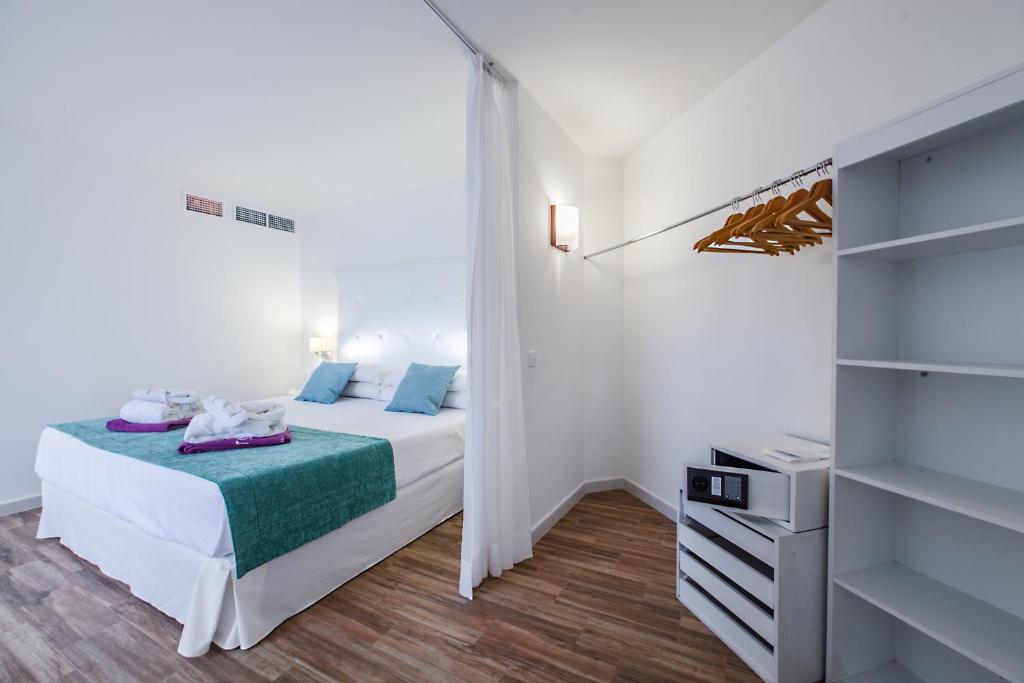 Mūsdienīga guļamistaba ar divguļamo gultu, baltu interjeru un koka grīdu. Uz gultas ir spilveni un dvieļi, kā arī skapī ir pakaramie un drošības seifs.