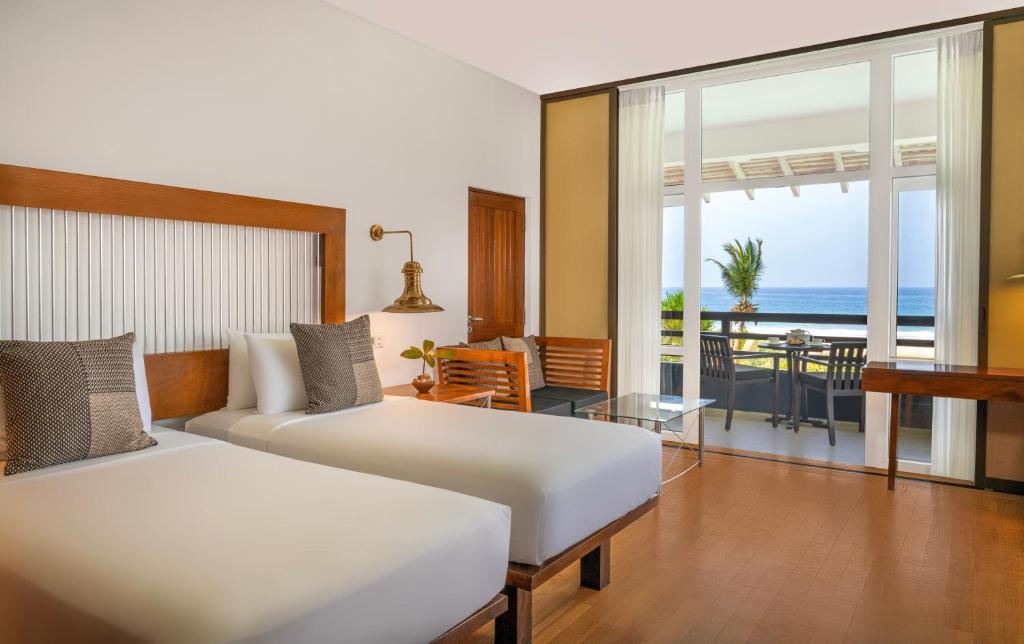 Mūsdienīga viesnīcas numura iekārtojums ar divām gultām un skatu uz jūru. Telpā ir koka mēbeles un lieli logi, kas nodrošina dabīgu apgaismojumu.