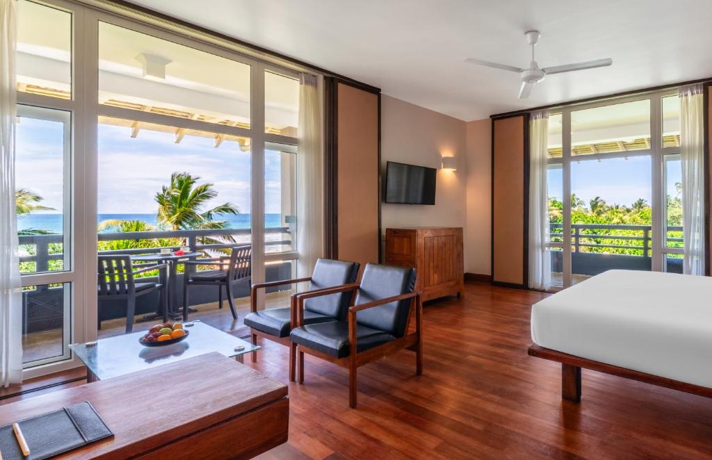 Mūsdienīgs viesnīcas numurs ar plašiem logiem, kas sniedzas līdz terasei, no kuras paveras skats uz okeānu un palmu ainavu. Numurā ir ērti krēsli, galda virsma un televizors.