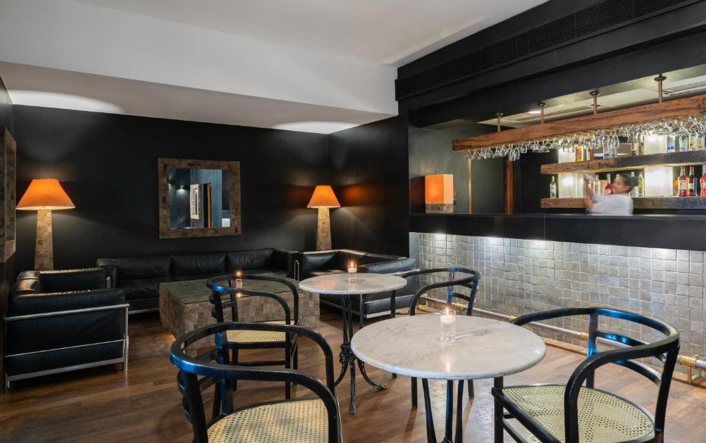 Mūsdienīgs bārs ar elegantām melnā krāsā krēslām un marmora galdiem, apgaismots ar siltām lampām. Bārā ir labi redzama dzērienu plauktu rinda ar dažādām pudelēm.